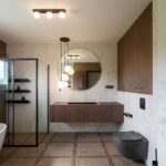 Zabudowa łazienki z wiszącą szafką i okrągłym lustrem De Morel