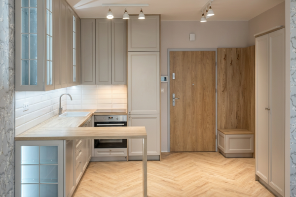 Beżowa kuchnia z przeszklonymi witrynami i półwyspem na wymiar De Morel